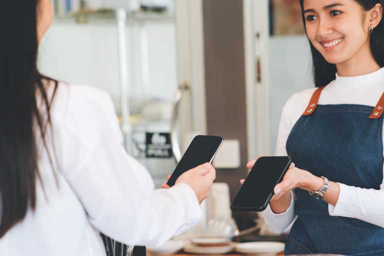 Mujer pagando por un cafe con su telefono por medio de tecnologia sin contacto