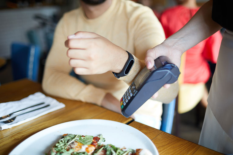 hombre pagando una pizza en un restaurante por medio de su reloj inteligente