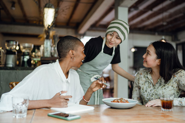 Dos mujeres clientes en un cafe hablando con la mesera